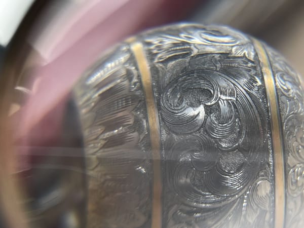 Detail of scrollwork and a gold band on a bolt knob through a magnifying glass