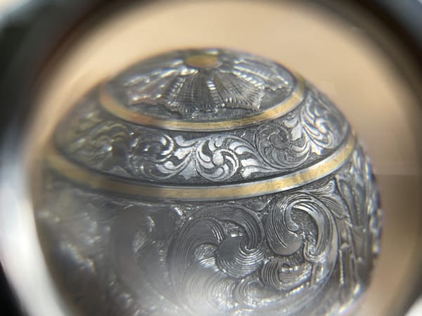 Bolt knob with acanthus scrollwork and gold bands seen through a magnifying glass
